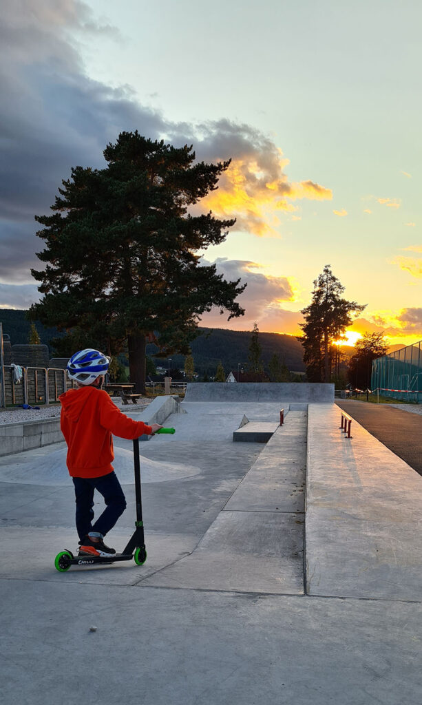 Barn på sparkesykkel ved skateparken i solnedgang.